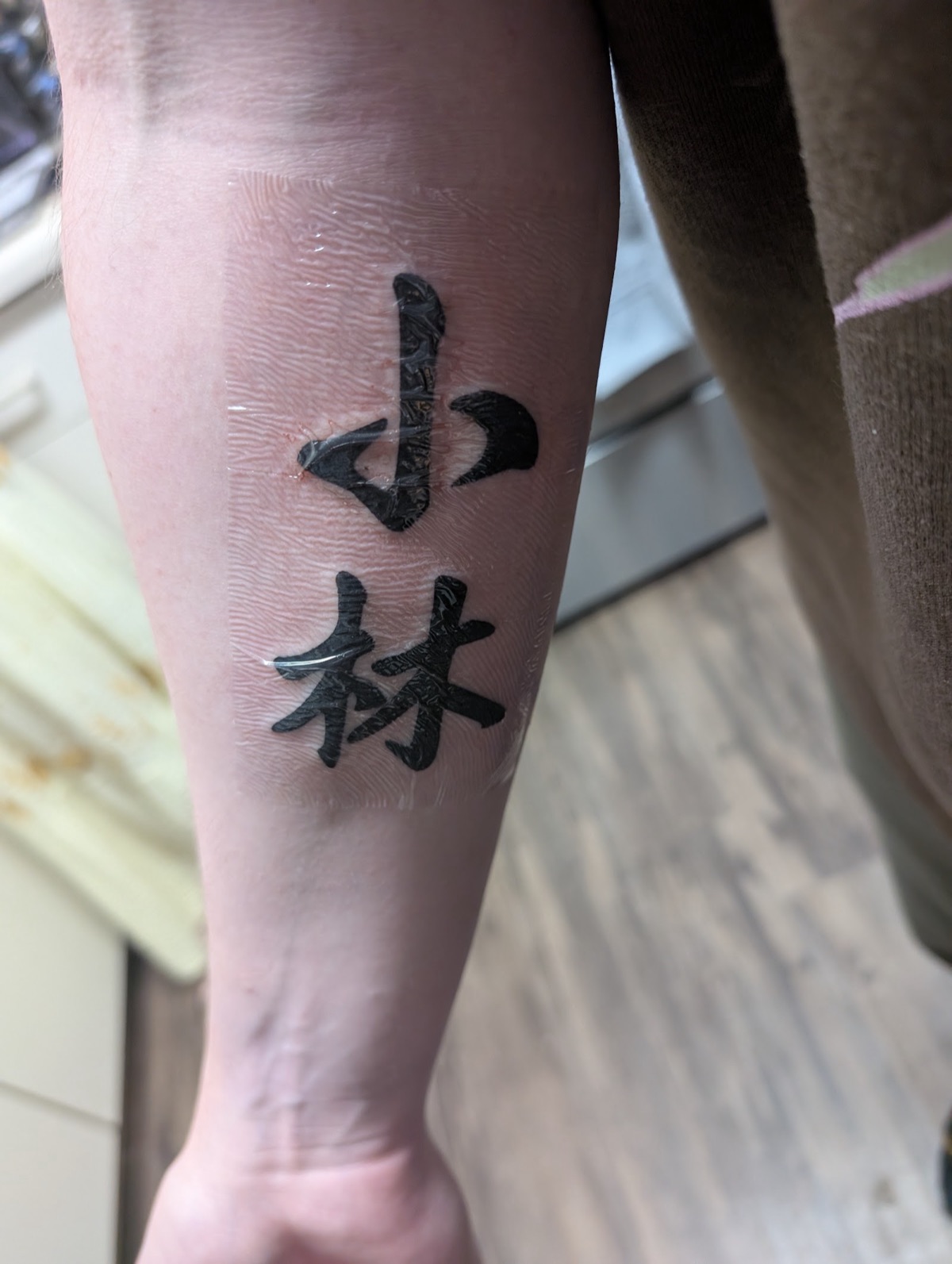 Two kanji characters tattooed in bold black on a forearm.
